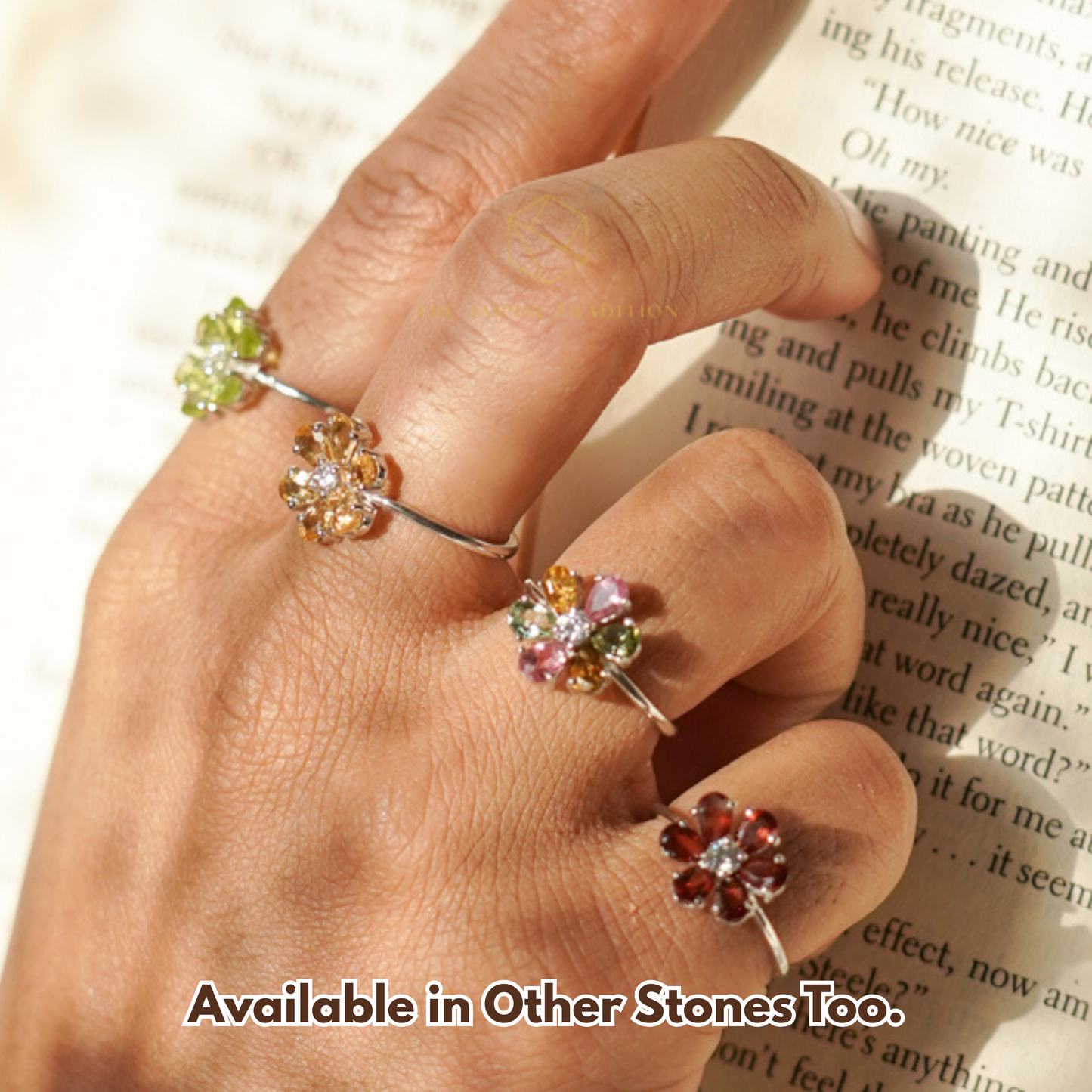 Hand wearing three floral silver rings with gemstones on a book page background