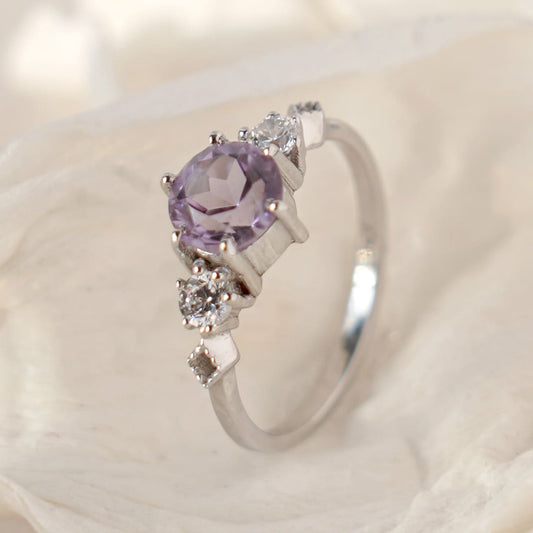 A silver ring with a round amethyst centerpiece and small sparkling accents on the sides, 