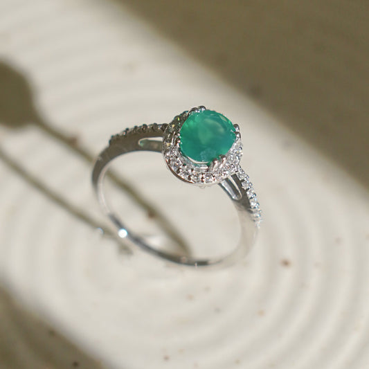 A silver ring with a central green onyx gemstone, with a delicate halo design.