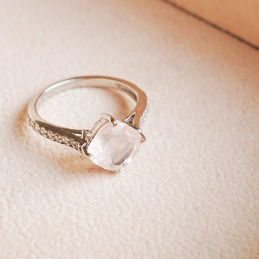 A close-up image of a silver ring with a natural rose quartz gemstone.