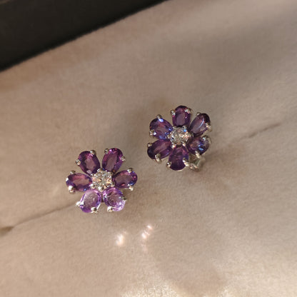 Pair of purple flower-shaped earrings on a beige surface