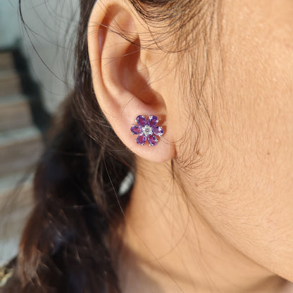 Close-up of an ear wearing a floral earring with purple stones.