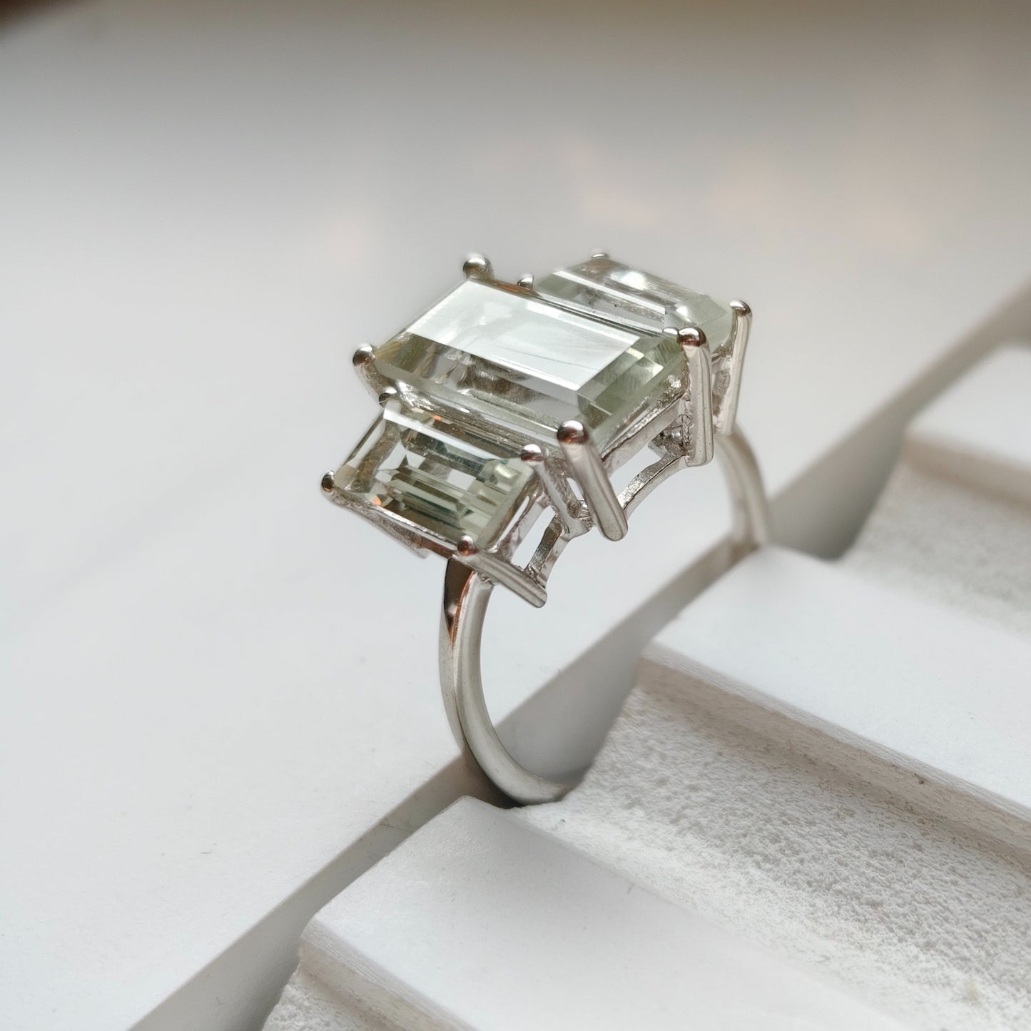 Silver ring with emerald-cut gemstones on a white surface