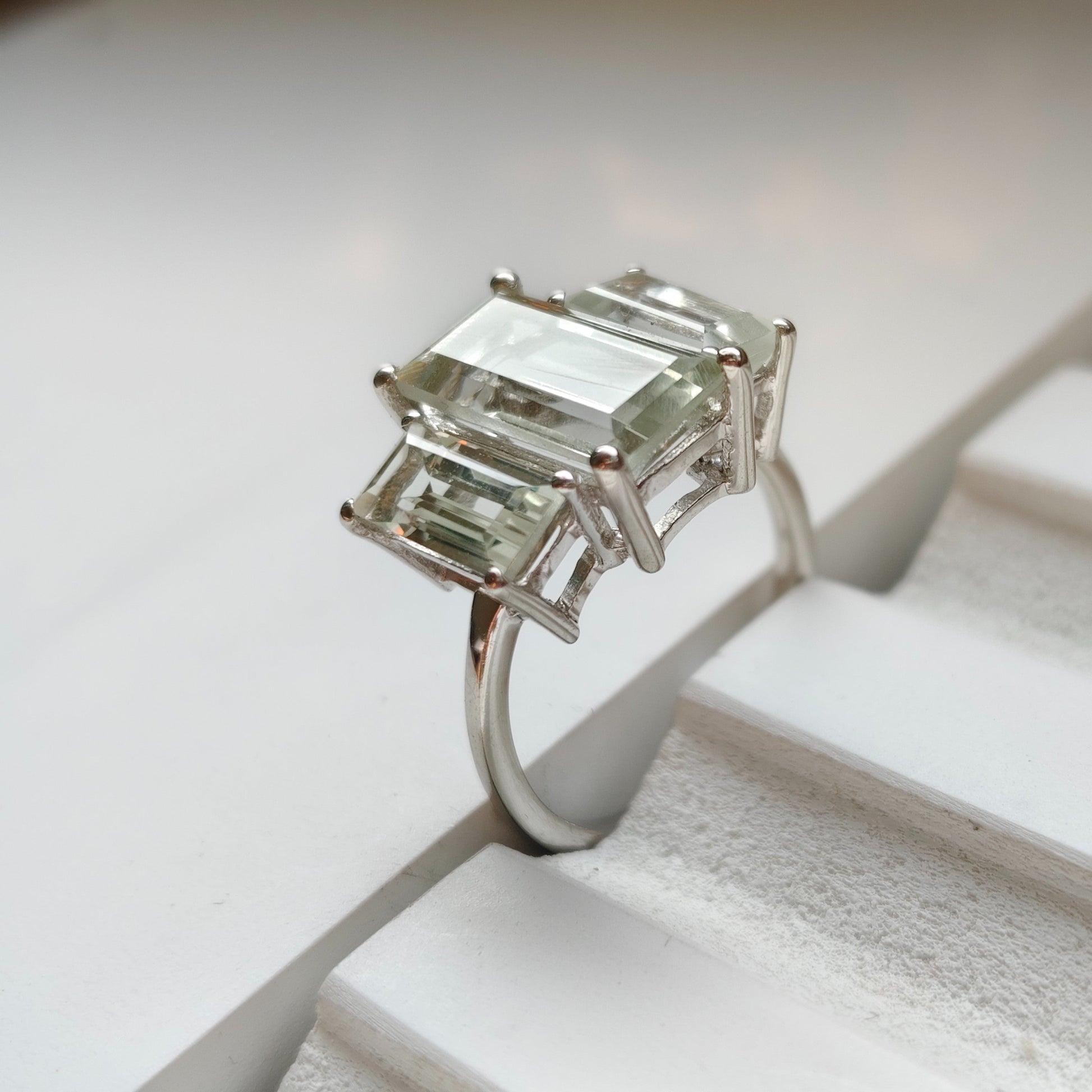 Silver ring with emerald-cut gemstones on a white surface