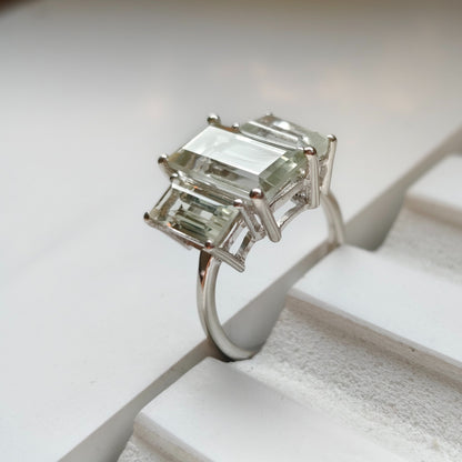 Silver ring with emerald-cut gemstones on a white surface