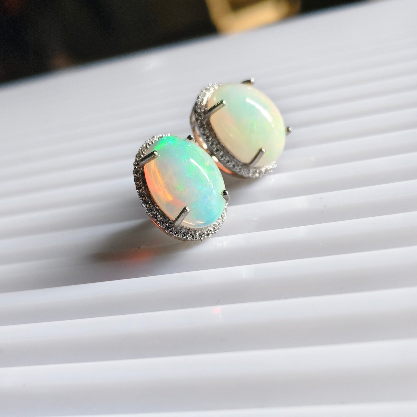 A pair of oval opal stud earrings with silver settings, resting on a white ribbed surface.