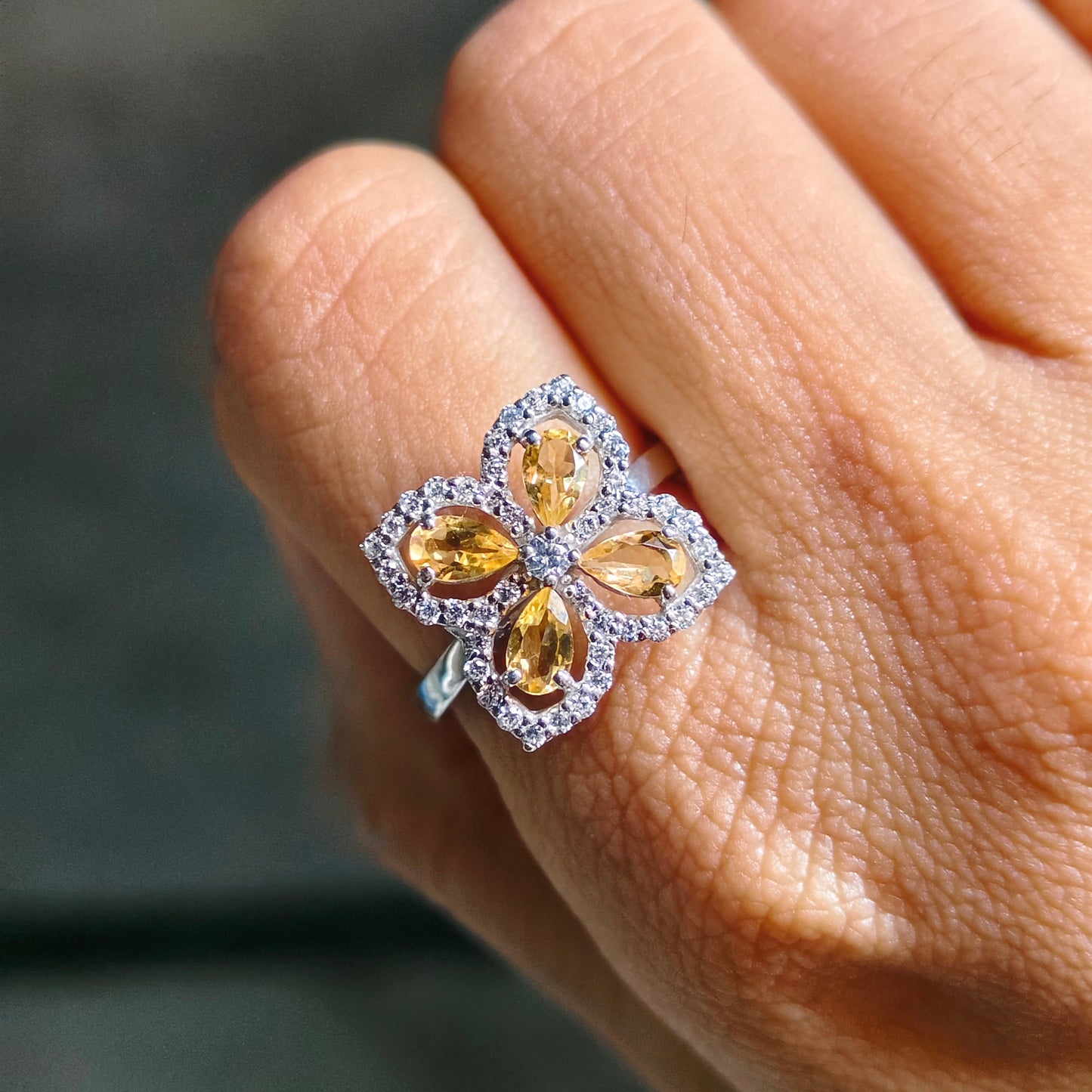 Close-up of a hand wearing a ring with four yellow gemstones on a blurred background