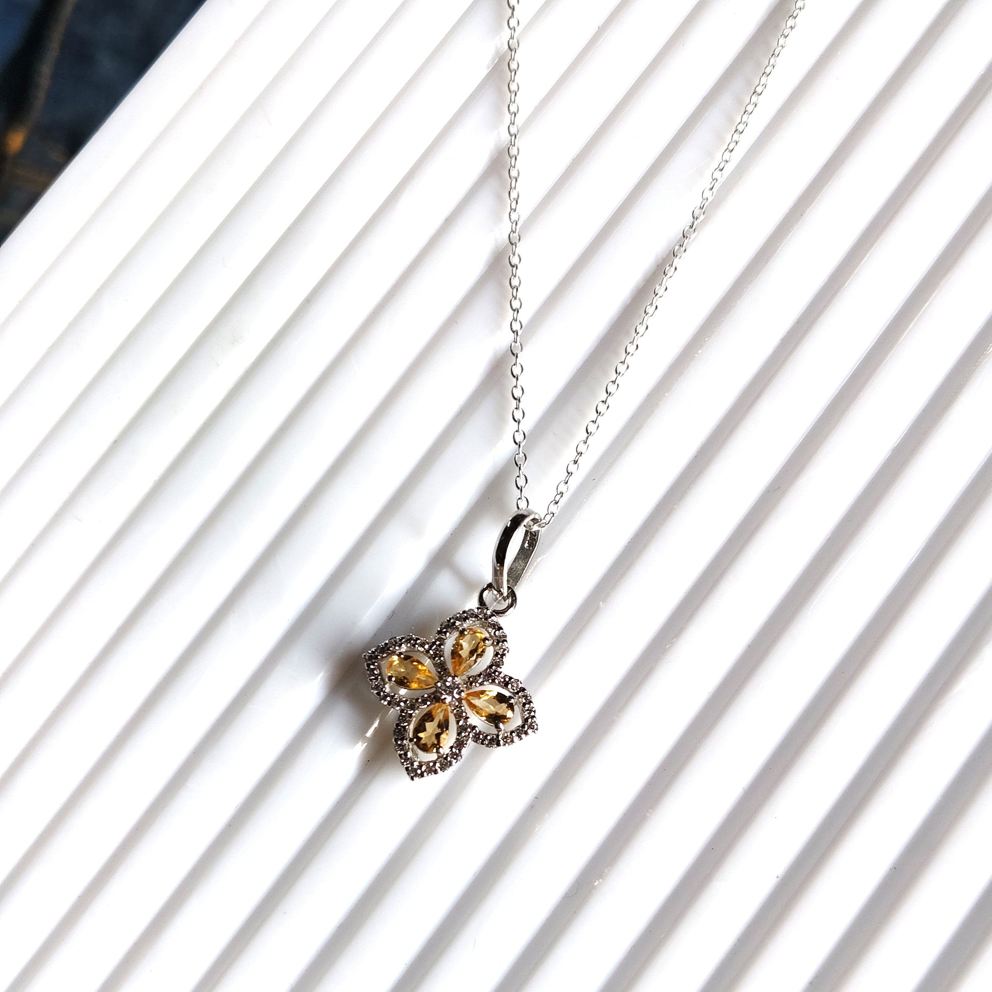 Silver necklace with a clover-shaped pendant on a white background