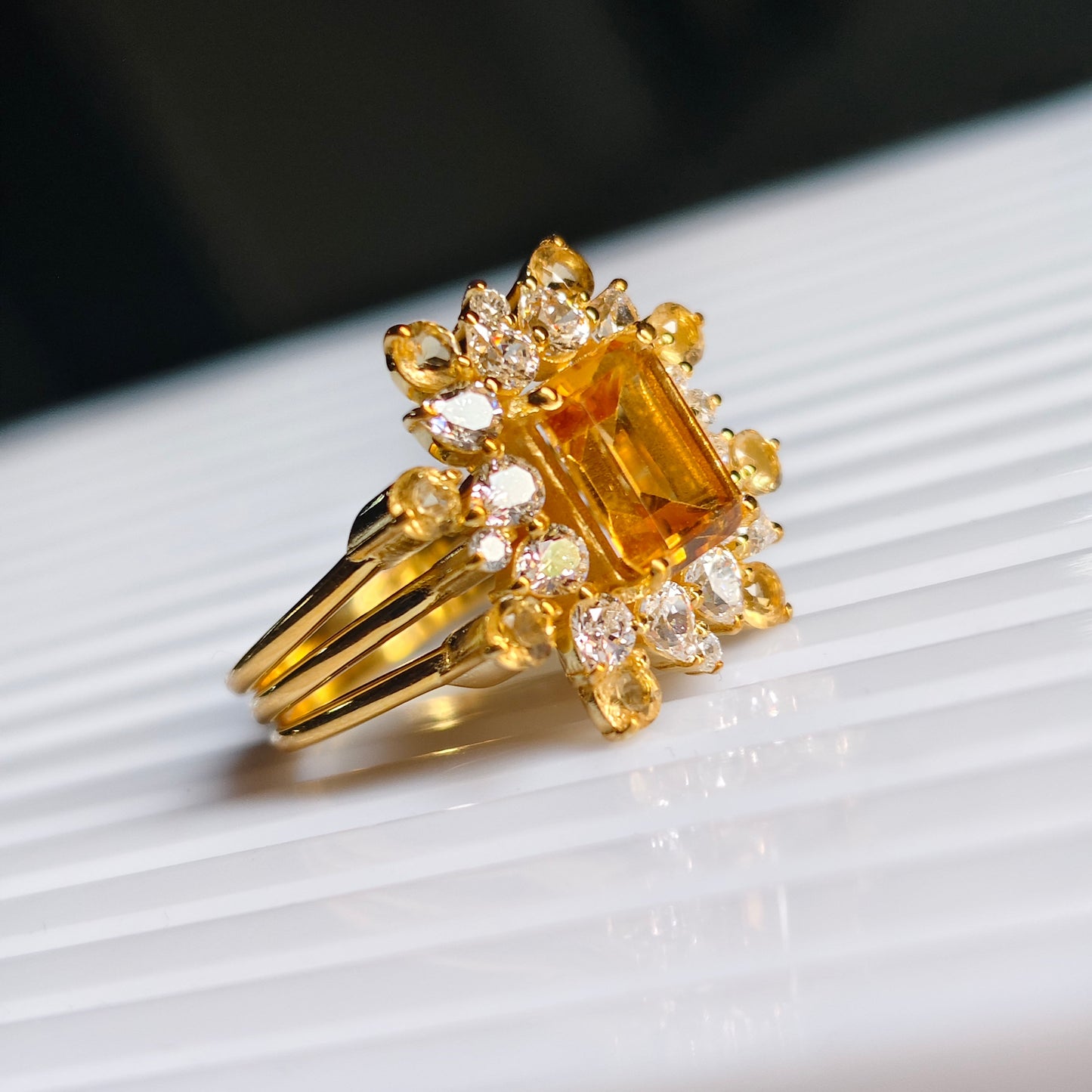 Gold ring with a large yellow gemstone and smaller diamonds on a white surface.