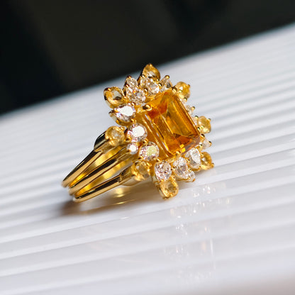 Gold ring with a large yellow gemstone and smaller diamonds on a white surface.
