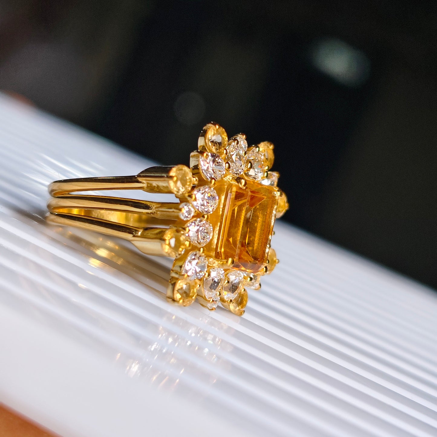 Gold ring with a large yellow gemstone and smaller diamonds on a white surface.