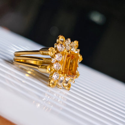 Gold ring with a large yellow gemstone and smaller diamonds on a white surface.