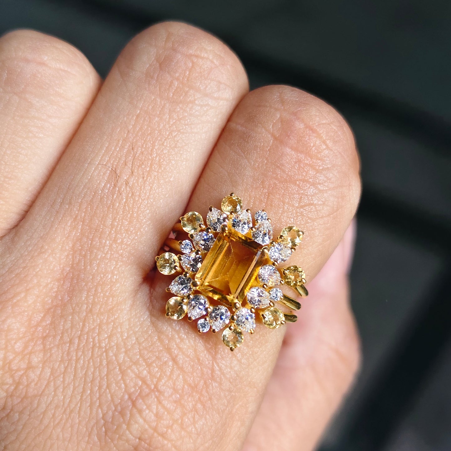 Gold ring with a central gemstone and smaller stones on a finger against a dark background