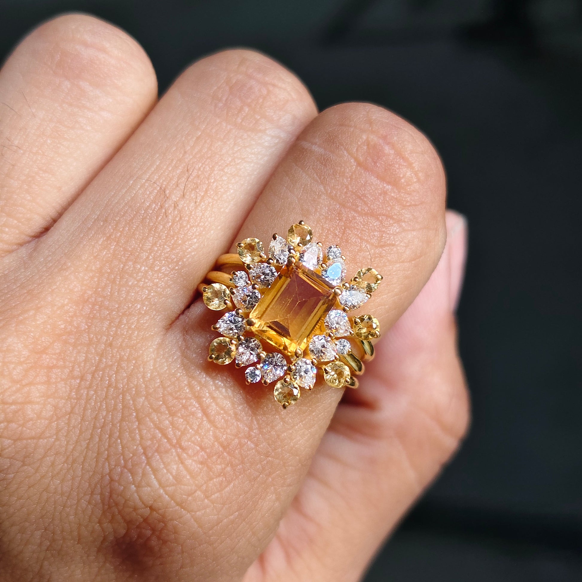 Gold ring with a large orange gemstone and smaller diamonds on a person's finger.