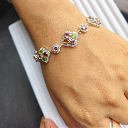 A close-up of a person's wrist wearing a silver-toned bracelet decorated with colorful gemstones, resting on a white ribbed surface.