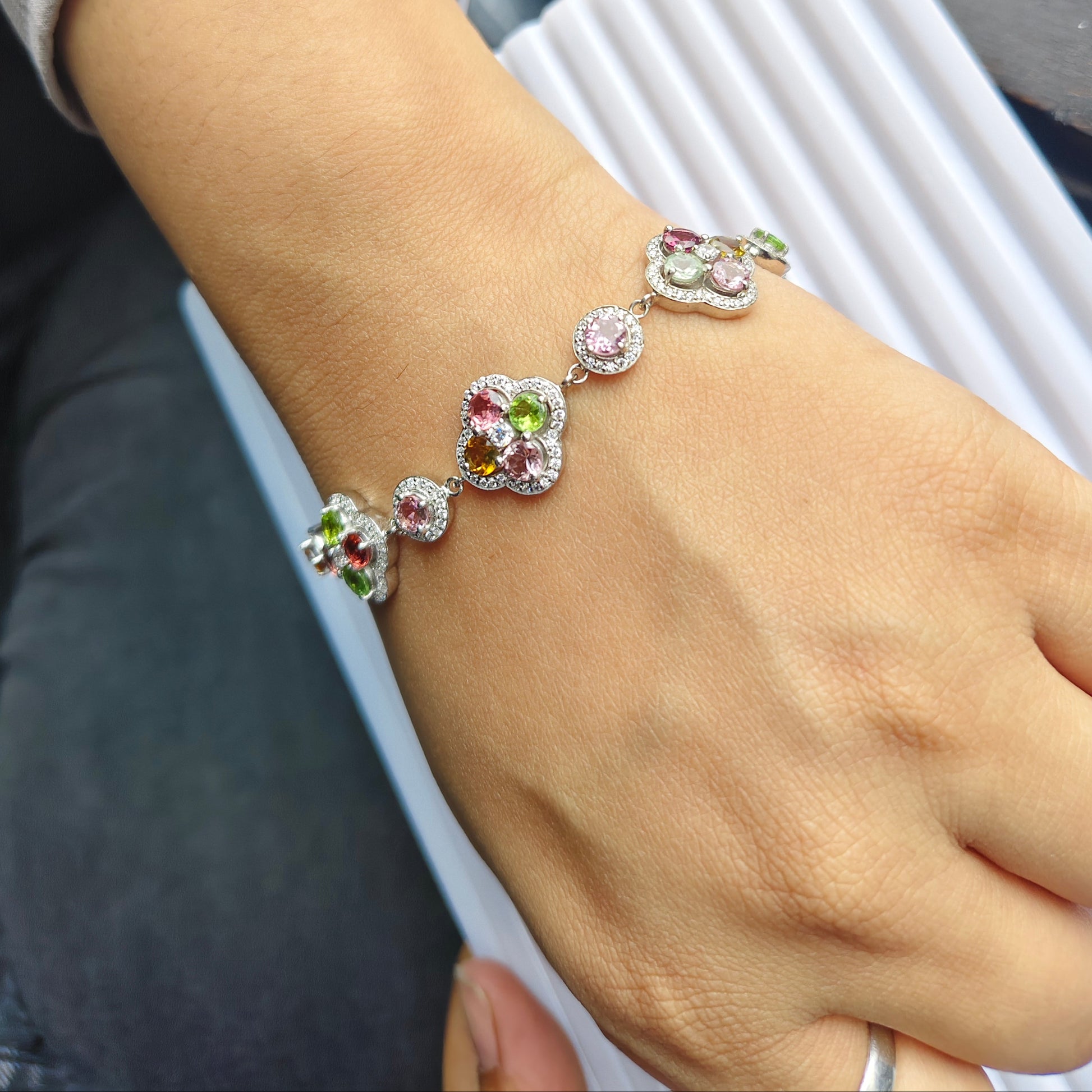 A close-up of a person's wrist wearing a silver-toned bracelet adorned with colorful gemstones, including pink, green, and purple accents, alongside a silver bangle.