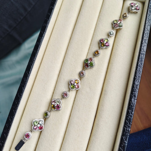 A delicate silver-toned bracelet with floral clusters of pink, green, and clear stones, displayed inside an open cream-colored jewelry box.