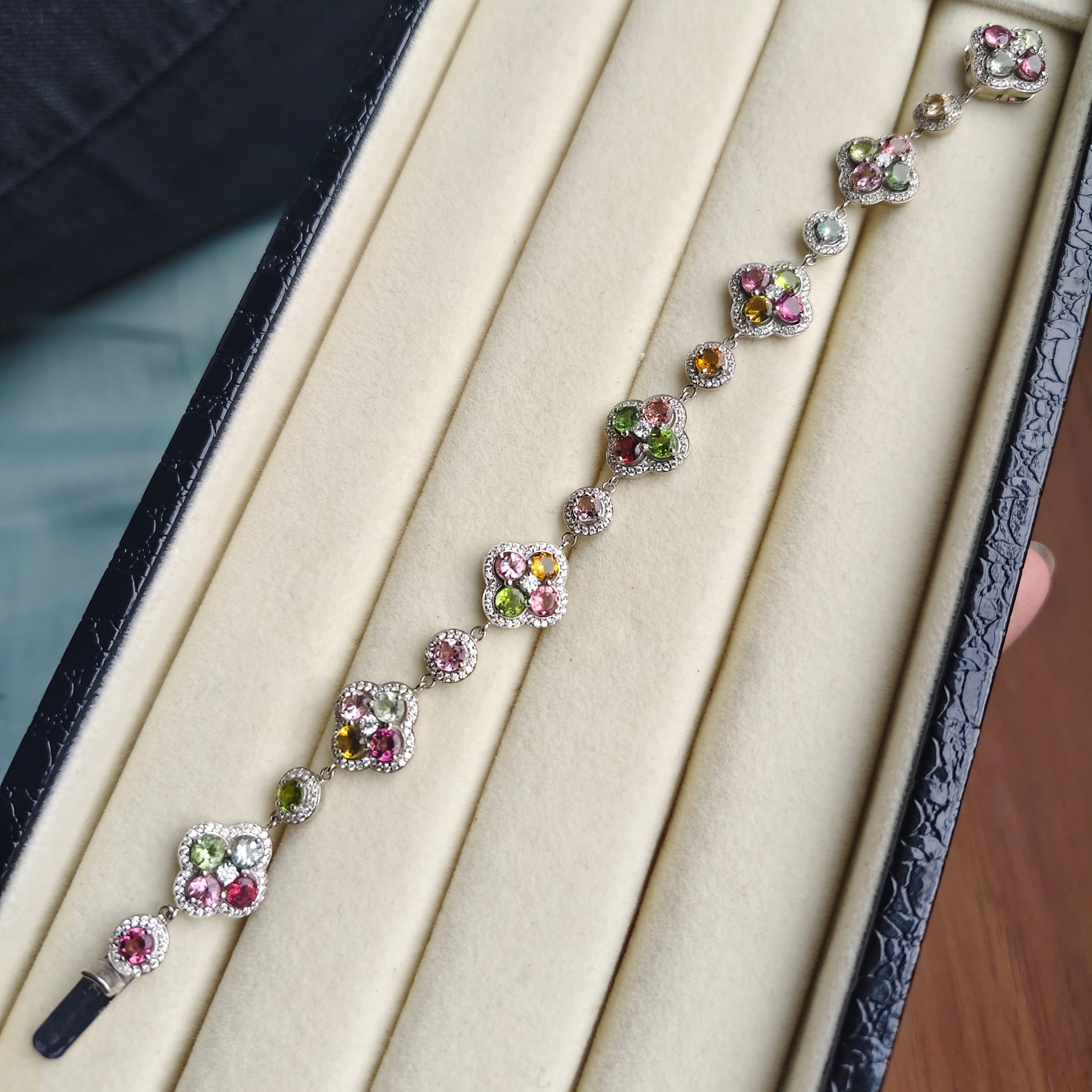 A floral silver-toned bracelet with colorful gemstones, displayed inside a black jewelry box with a beige velvet interior.
