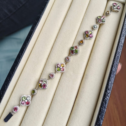 A floral silver-toned bracelet with colorful gemstones, displayed inside a black jewelry box with a beige velvet interior.