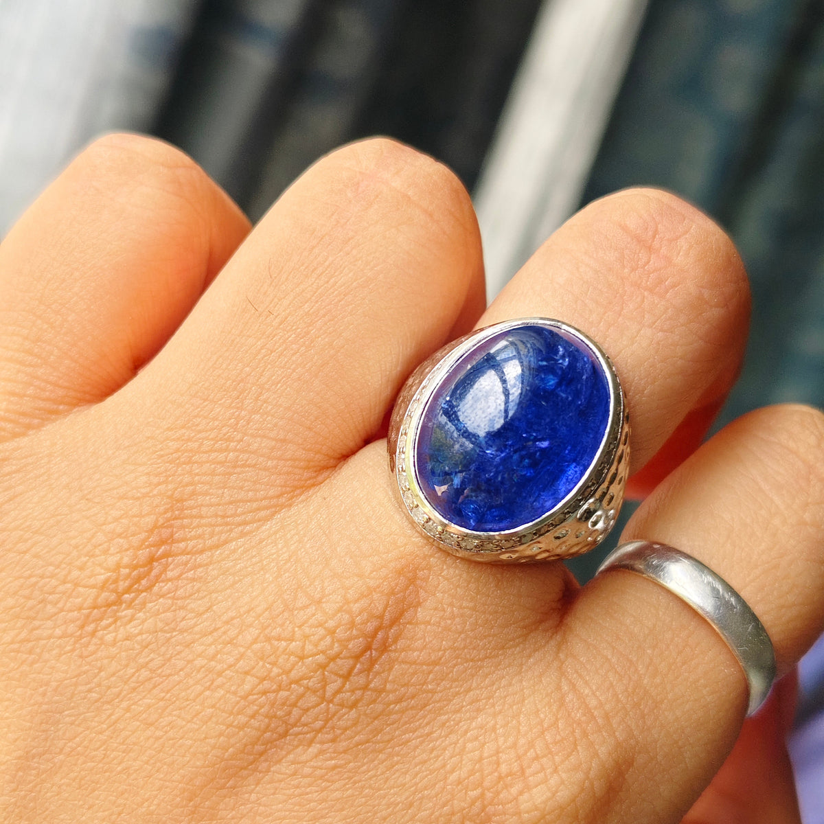 A silver ring with a large oval blue lapis lazuli stone, worn on a finger. A simple silver band is also visible on the same finger.