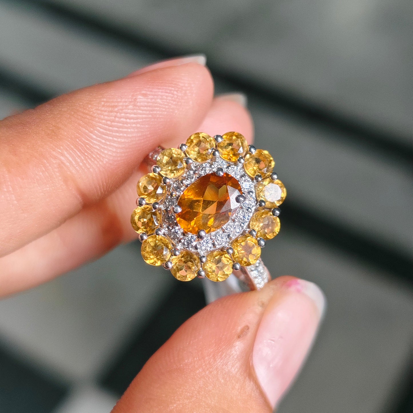 A close-up of a hand holding a silver ring with a large oval yellow center stone and multiple round yellow accent stones in a halo setting.