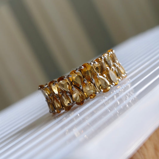 A gold ring featuring a row of marquise-cut amber gemstones, resting on a white ribbed surface with a softly blurred background.