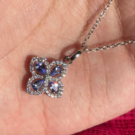 A silver butterfly pendant necklace with purple gemstones, resting on a person's palm over a bright pink textured fabric.