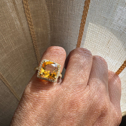 Hand wearing a ring with a yellow gemstone against a neutral background