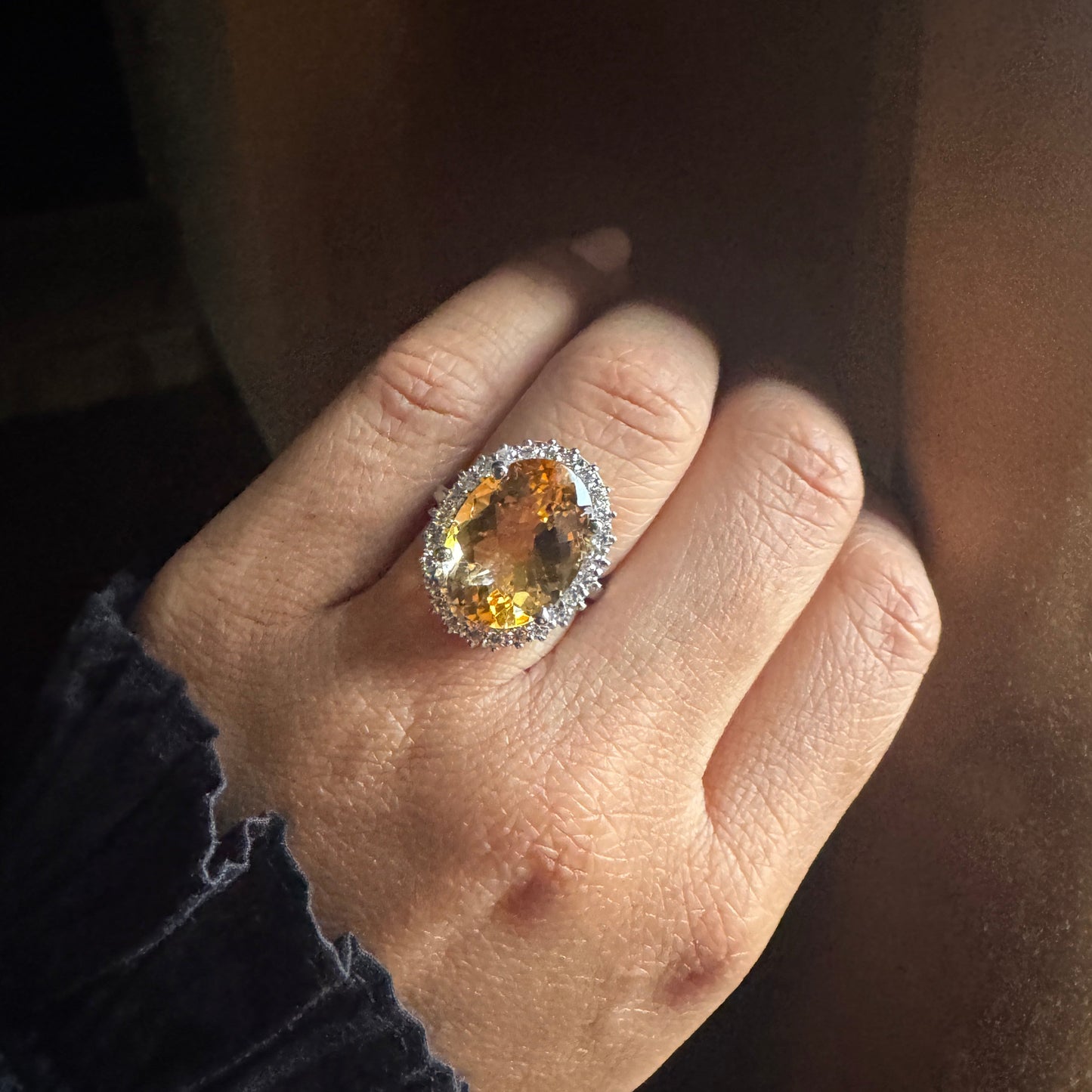 Hand wearing a ring with a large gemstone against a dark background