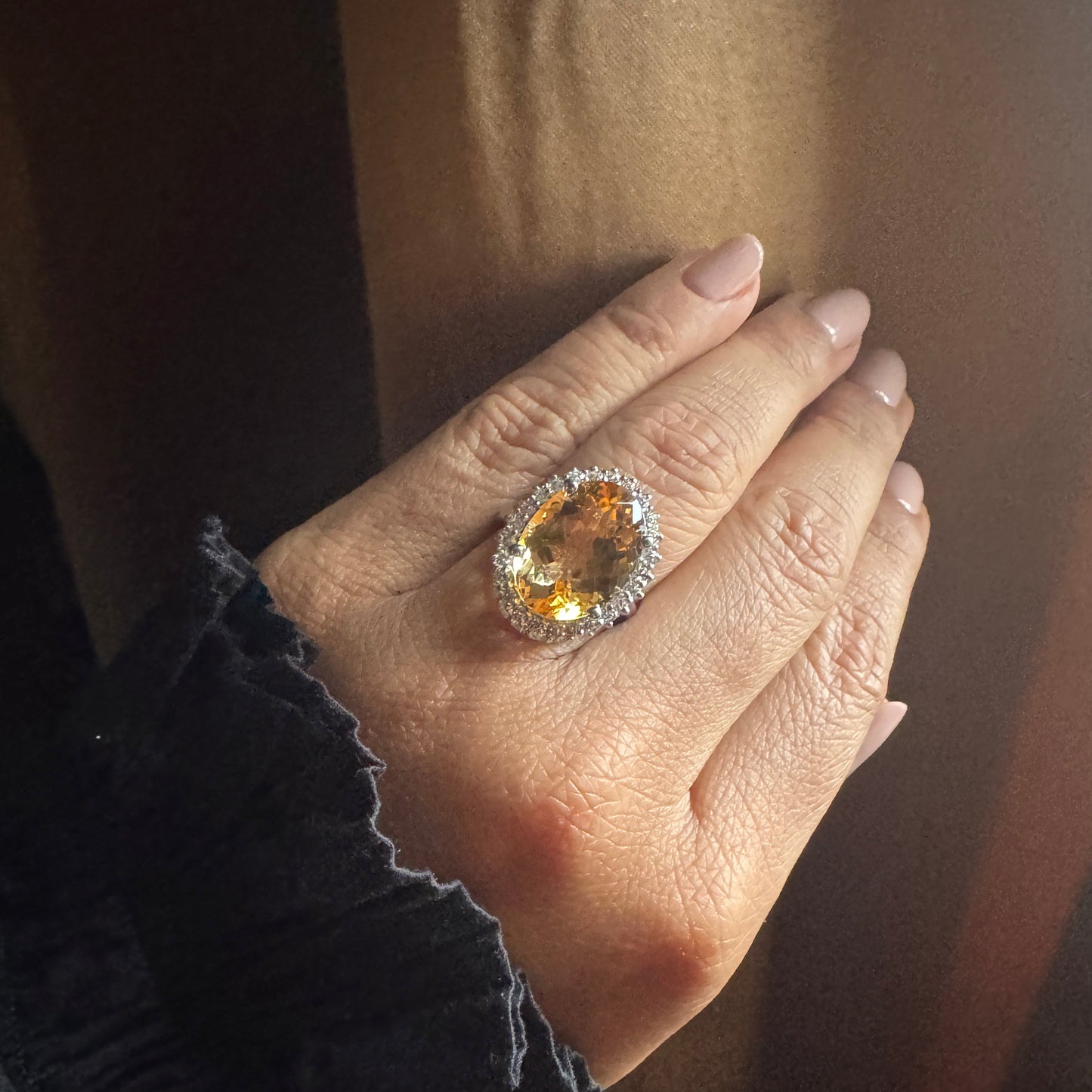 Hand wearing a ring with a large orange gemstone against a neutral background