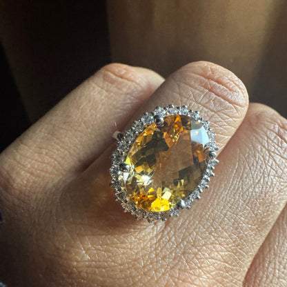 Close-up of a hand wearing a ring with a large yellow gemstone.
