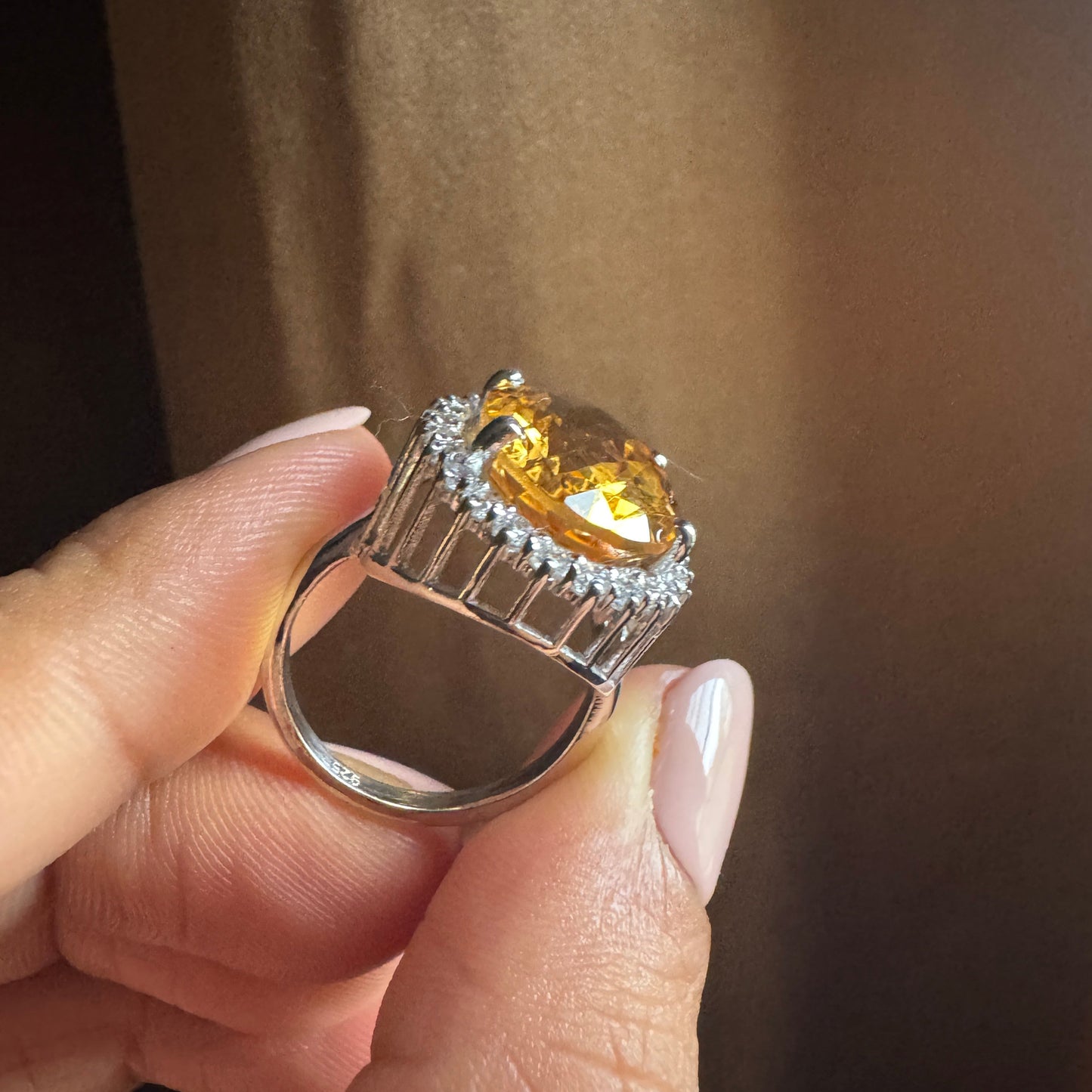 Ring with a yellow gemstone held by a hand against a brown background