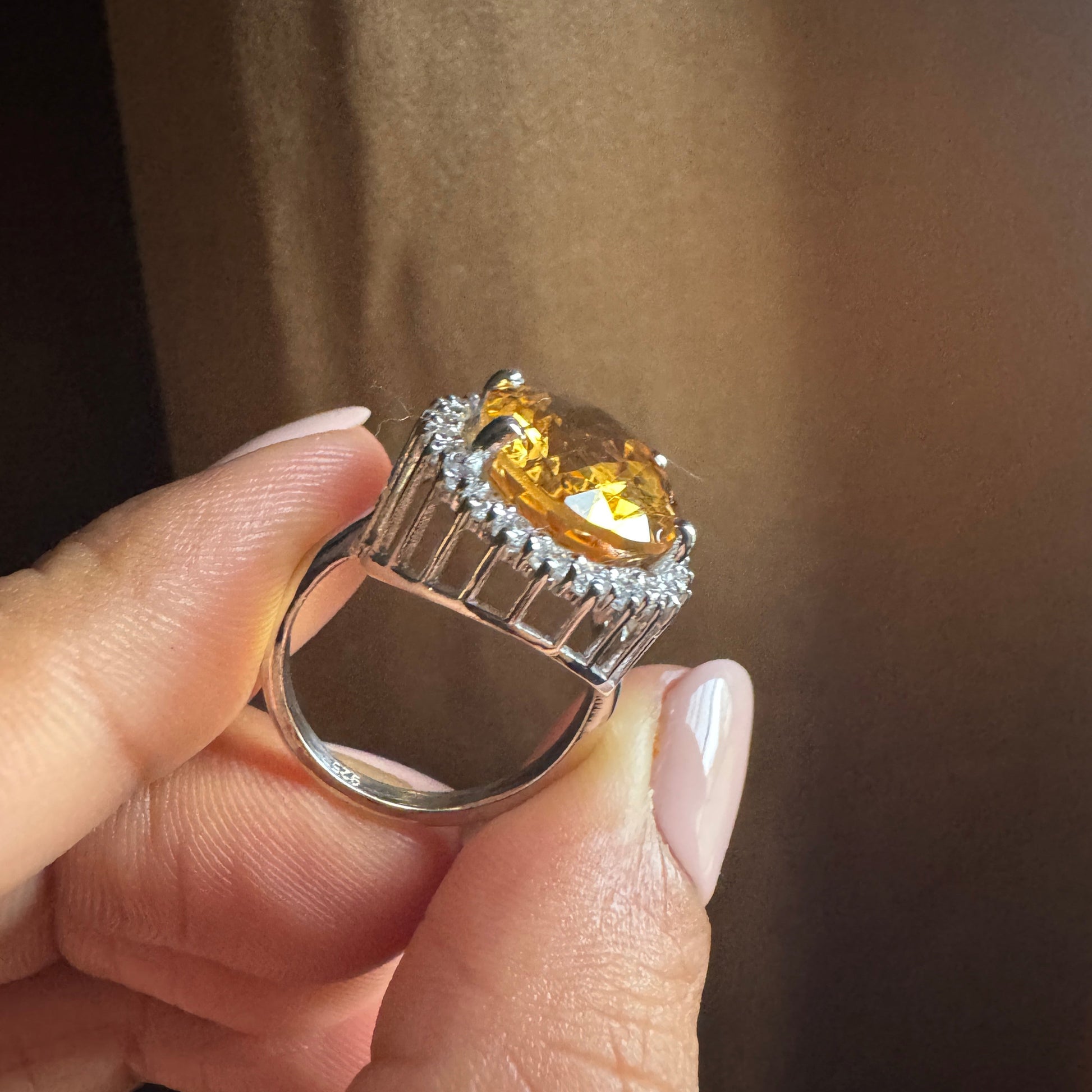 Ring with a yellow gemstone held by a hand against a brown background