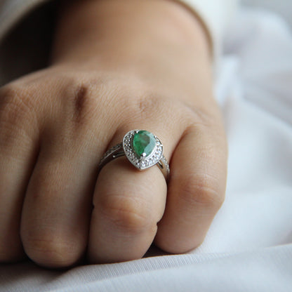 Hand wearing a ring with a green gemstone on a white fabric background