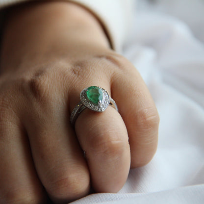 Close-up of a hand wearing a ring with a green gemstone on a white background