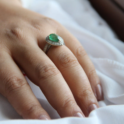 Hand wearing a ring with a green gemstone on a white fabric background
