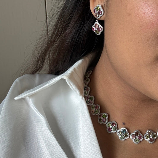 A close-up lifestyle shot of a woman wearing a matching silver-toned jewelry set featuring a necklace and matching stud earrings with pink and green gemstone accents.