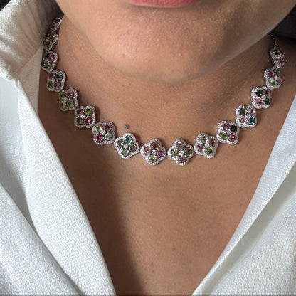A close-up lifestyle shot of a model wearing a silver-toned necklace with small pink and green enamel floral details, paired with a white collared shirt.