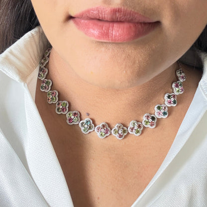 A close-up lifestyle shot of a person wearing a silver-toned floral choker necklace with colorful rhinestone accents, styled with a white satin shirt.