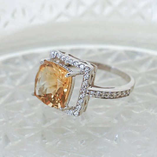 A silver ring with a square citrine center stone surrounded by smaller cubic zirconia stones.