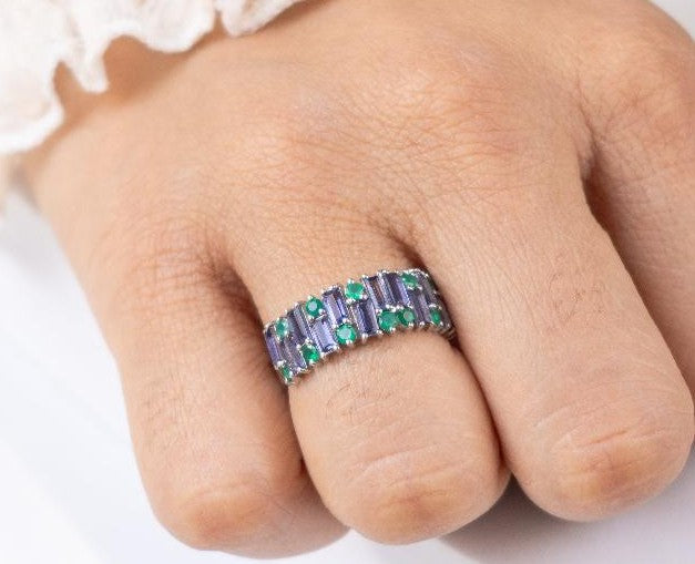 Close-up of a hand wearing a ring with purple and green gemstones on a white background