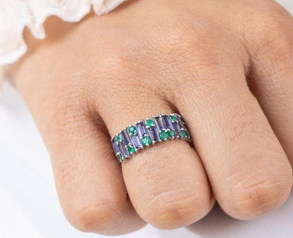 Close-up of a hand wearing a ring with purple and green gemstones on a white background